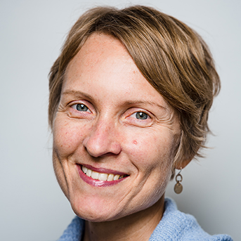 The image shows a closeup headshot of Tara Fischer with short dirty blonde hair, smiling. They are wearing a light blue top with gold dangle earrings.