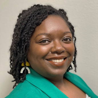 The image shows a headshot of Martina Durant with medium dark hair, smiling. They are wearing a collared green blazer.