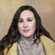 Kim Grice, a woman with long wavy brown hair, wearing a beige coat and a light gray turtleneck sweater, poses against a plain, softly blurred background. She has a neutral expression and appears to be looking directly at the camera.